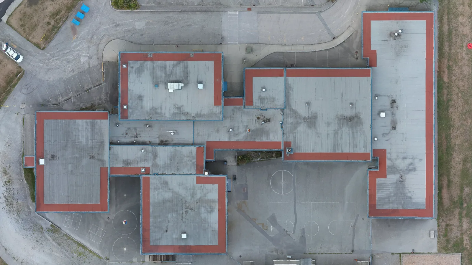 RGB drone orthomosaic of a multi-wing low-slope commercial roof from directly above, captured with a DJI Matrice 30T, showing parapets, roof hatches and rooftop units.