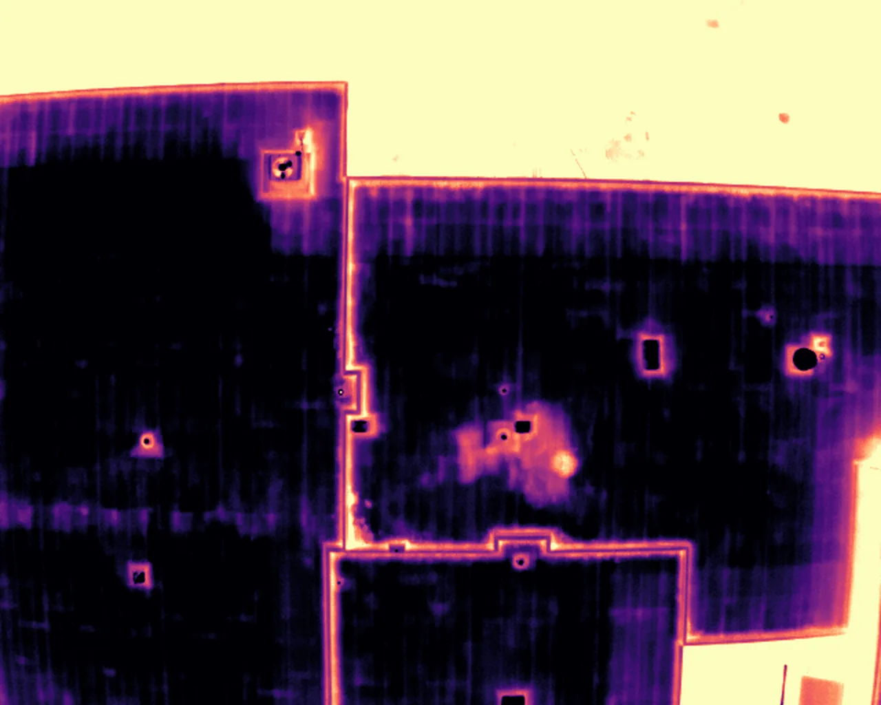 Radiometric thermal frame of a low-slope commercial roof captured after dark with a DJI Matrice 30T. Magma palette over a 12.5 to 18 degree Celsius display range: dark is cooler, light is warmer. No annotation.